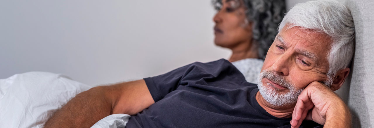 A  concerned older man in bed looking away from his partner