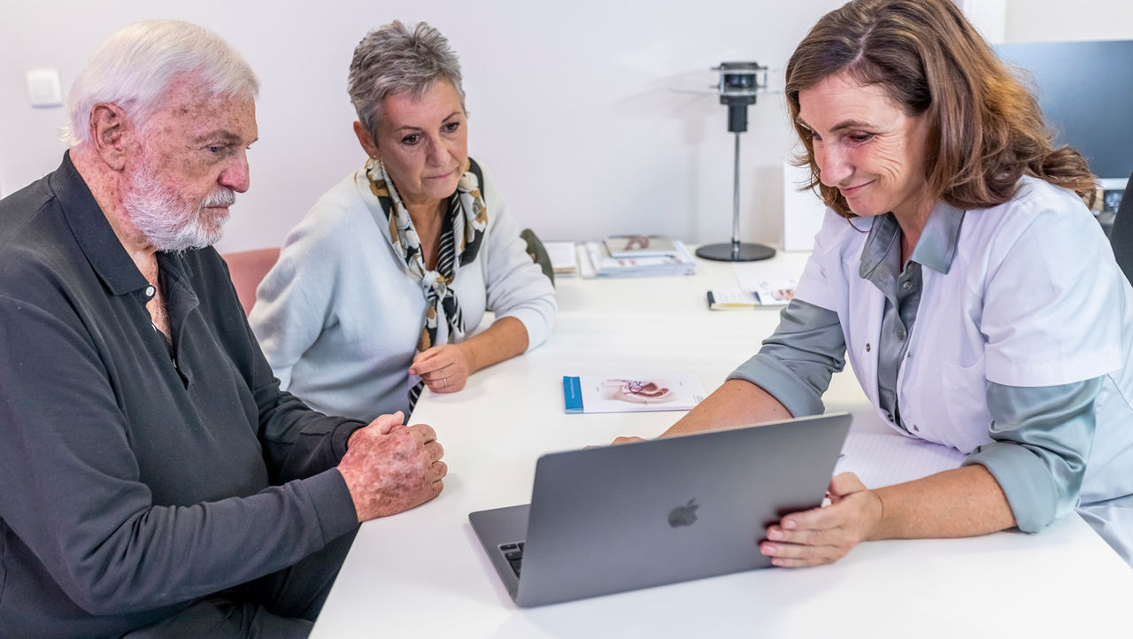 A physician reassuring an elderly male patient who is sitting across a table from her.