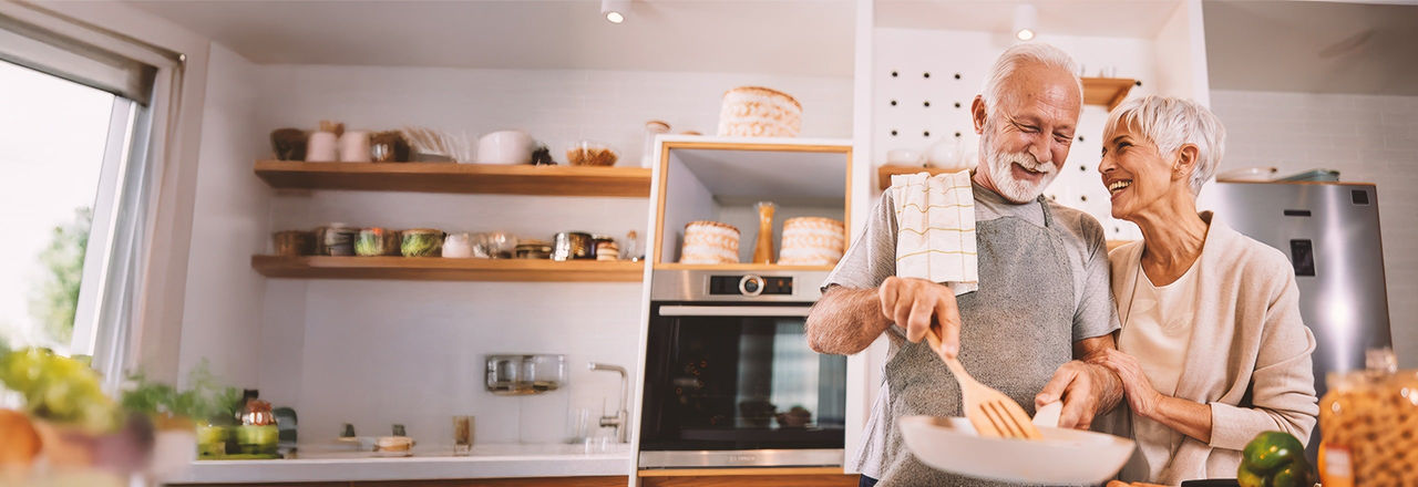 Older couple cooking in kitchen talking about enlarged prostate