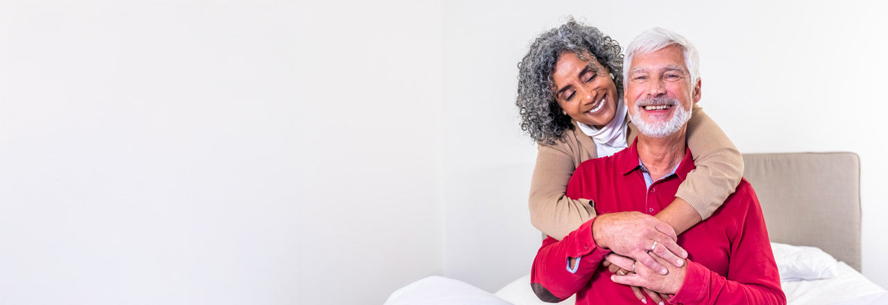 An older woman embraces her male partner from behind