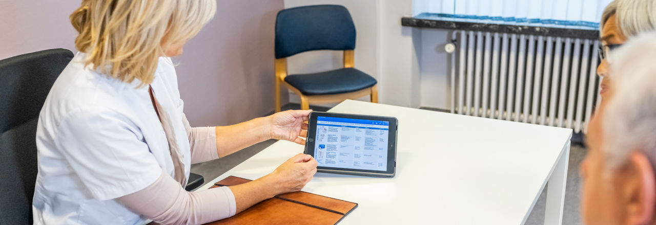 A doctor holds a tablet showing some text for an older man to see.